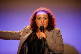 Mirela Pascu pe scena evenimentului From Finish to Start, vara lui 2014, cu microfonul în mână și cablul strâns colac pe degetul mic
